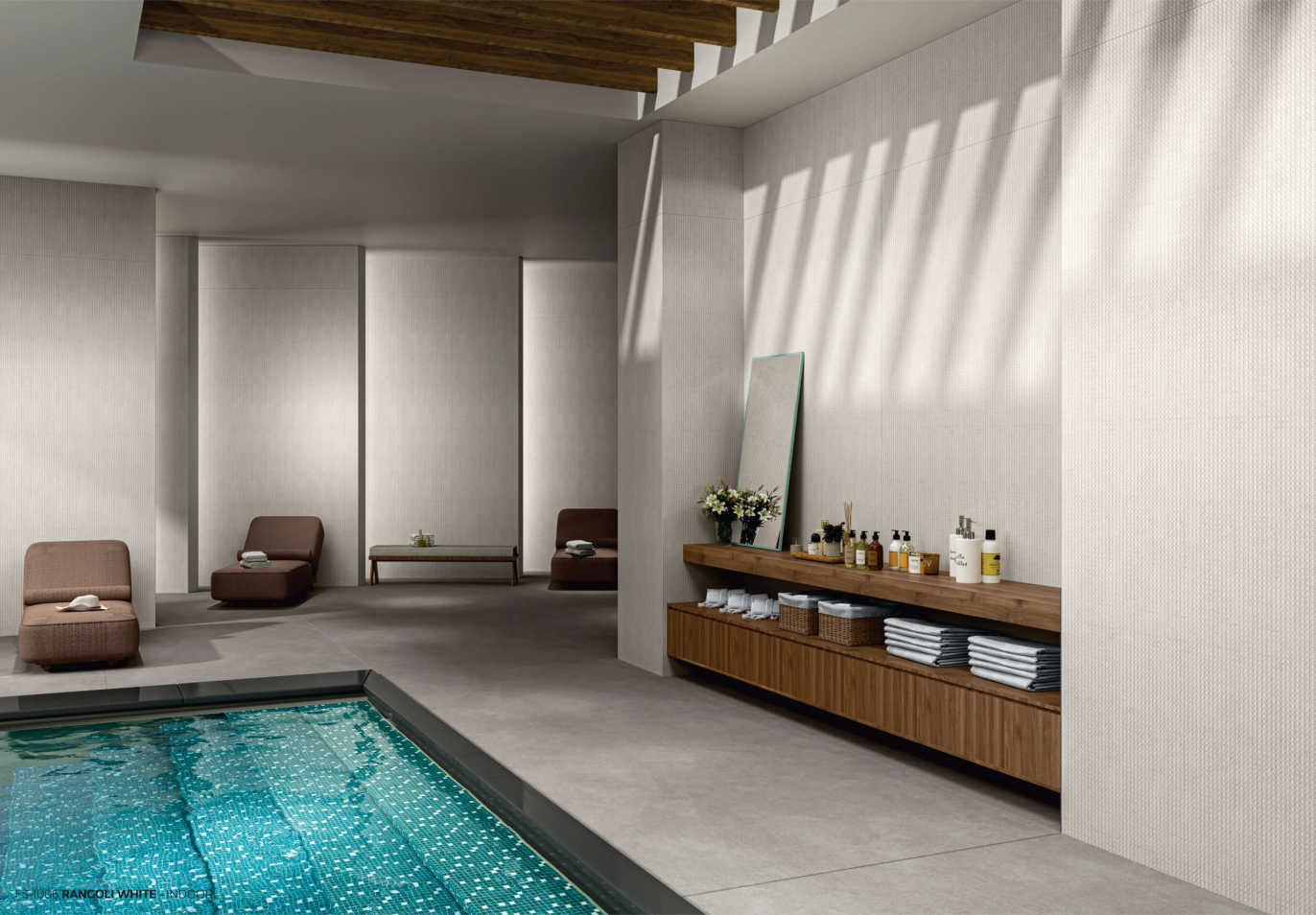 Modern indoor spa lounge featuring a tiled pool, minimalist brown lounge chairs, a wooden ceiling accent, and a sleek wooden counter with towels, toiletries, and a mirror against light-textured walls.